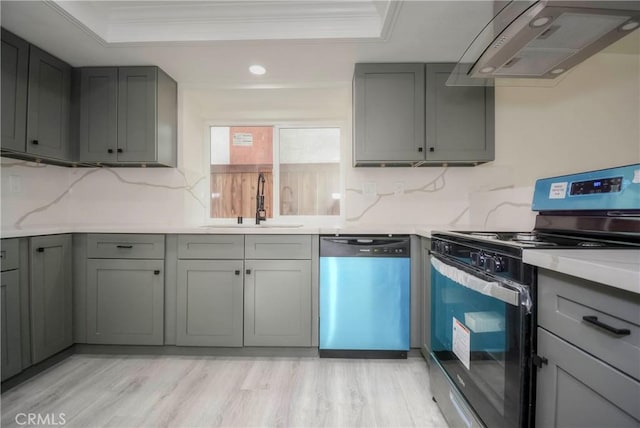 kitchen featuring appliances with stainless steel finishes, a tray ceiling, sink, and wall chimney range hood