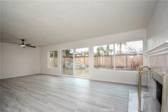 unfurnished sunroom featuring ceiling fan and a tiled fireplace