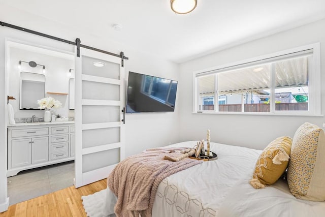 bedroom with a barn door, sink, and light hardwood / wood-style floors