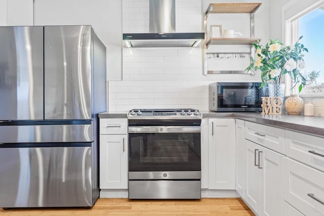 kitchen featuring light hardwood / wood-style flooring, stainless steel appliances, white cabinets, decorative backsplash, and wall chimney exhaust hood