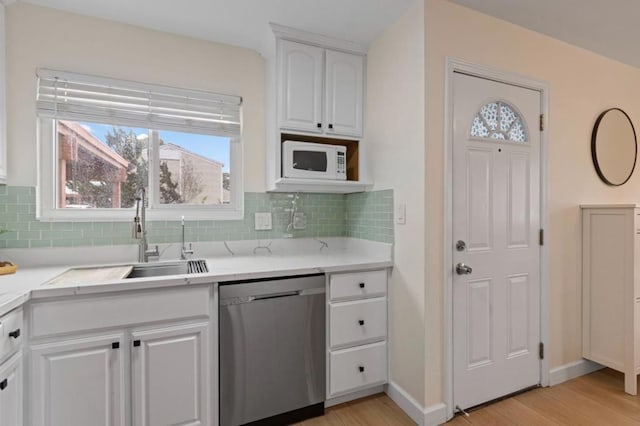 kitchen with white cabinetry, sink, backsplash, stainless steel dishwasher, and light hardwood / wood-style floors