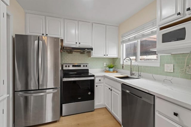 kitchen featuring sink, appliances with stainless steel finishes, light stone counters, white cabinets, and light wood-type flooring