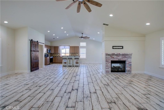 unfurnished living room featuring a fireplace, a barn door, vaulted ceiling, and light hardwood / wood-style flooring