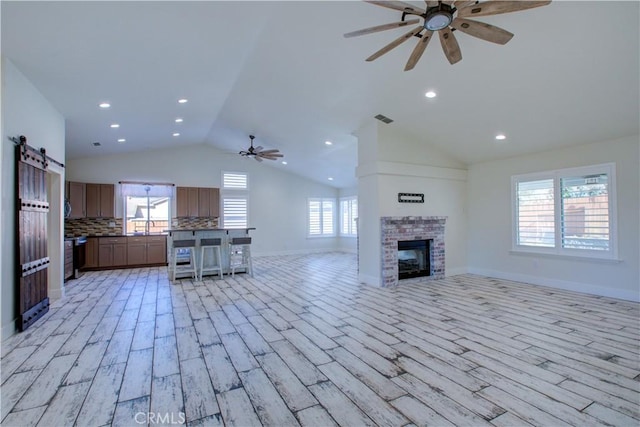 unfurnished living room featuring a brick fireplace, light hardwood / wood-style floors, a barn door, and ceiling fan