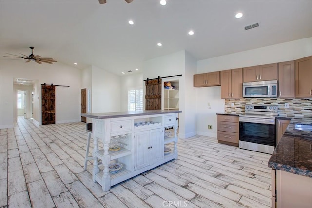 kitchen featuring stainless steel appliances, vaulted ceiling, a barn door, and ceiling fan