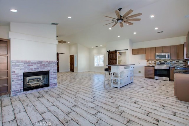 kitchen featuring lofted ceiling, tasteful backsplash, ceiling fan, stainless steel appliances, and a barn door