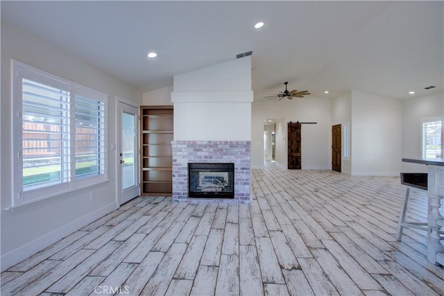 unfurnished living room featuring lofted ceiling, light hardwood / wood-style flooring, a barn door, and ceiling fan