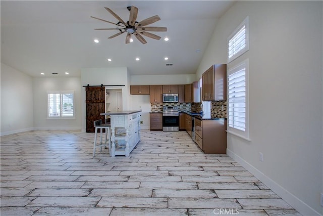 kitchen featuring a kitchen bar, appliances with stainless steel finishes, ceiling fan, a barn door, and backsplash