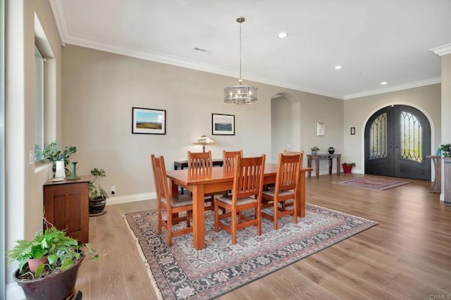 dining area with arched walkways, baseboards, french doors, light wood finished floors, and crown molding