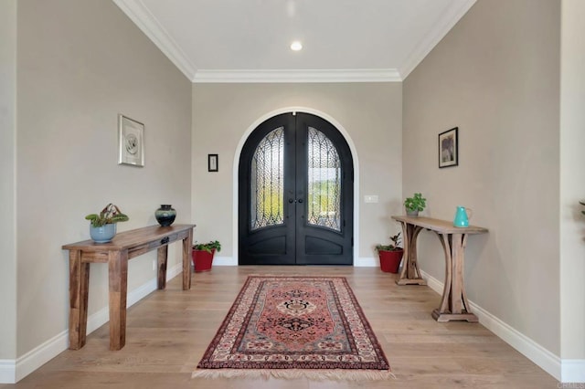 foyer entrance featuring arched walkways, baseboards, french doors, ornamental molding, and light wood-type flooring