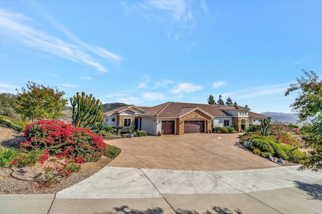 ranch-style home with an attached garage, a mountain view, concrete driveway, and a tiled roof