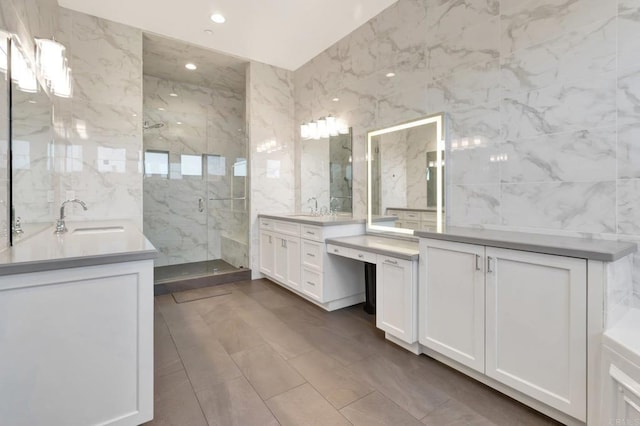 full bathroom with a marble finish shower, tile walls, two vanities, and a sink