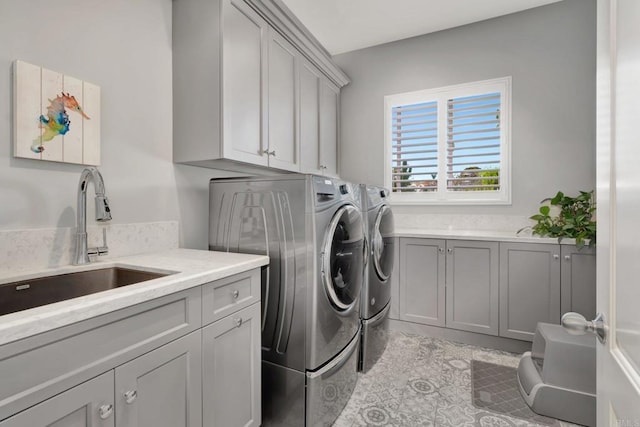 clothes washing area featuring washing machine and dryer, cabinet space, and a sink