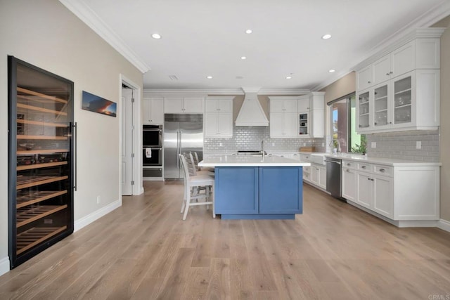 kitchen featuring white cabinets, glass insert cabinets, custom exhaust hood, stainless steel appliances, and light countertops