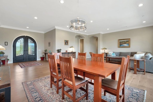 dining space featuring arched walkways, french doors, a chandelier, and light wood-style flooring