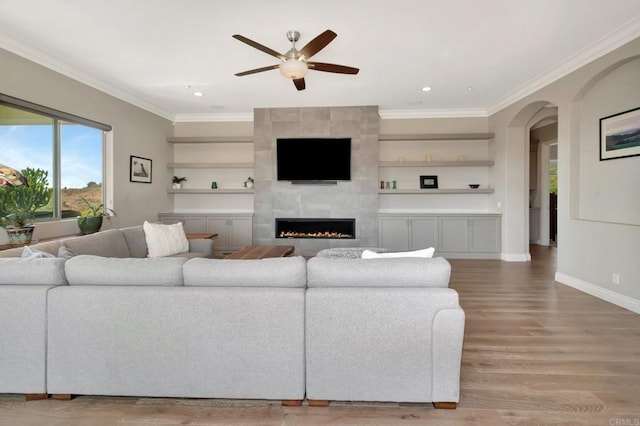 living area featuring arched walkways, crown molding, a tiled fireplace, and wood finished floors