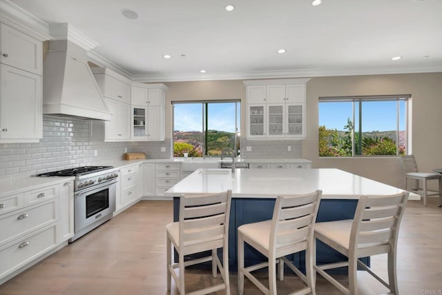 kitchen featuring glass insert cabinets, high end stove, light countertops, and a center island with sink