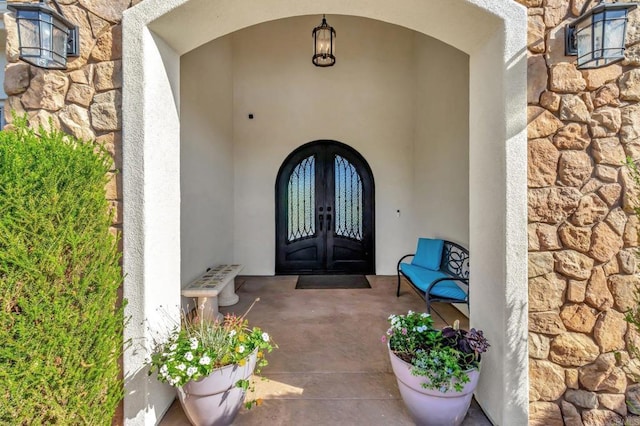 property entrance with stone siding, stucco siding, and french doors