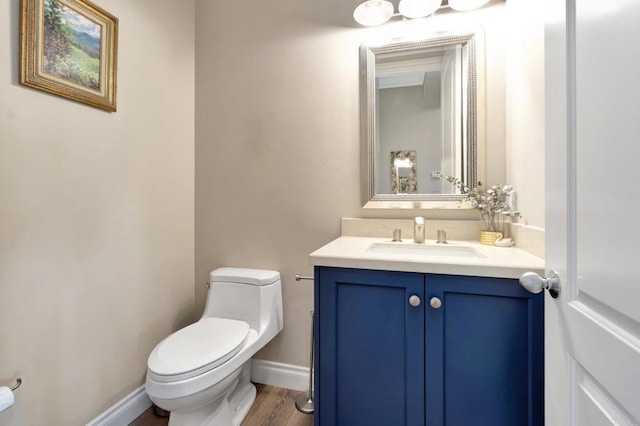 half bathroom with toilet, baseboards, wood finished floors, and vanity