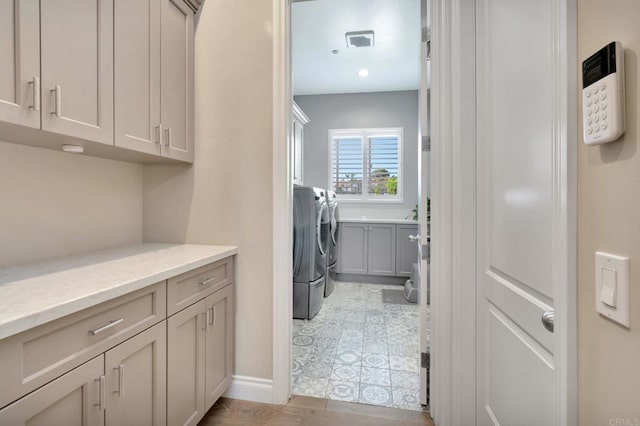 clothes washing area with washer and dryer, cabinet space, and visible vents