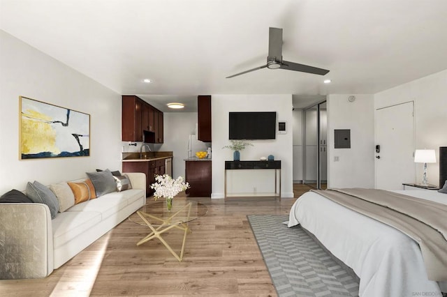 bedroom with sink, electric panel, ceiling fan, and light hardwood / wood-style flooring