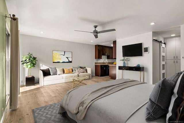 bedroom with ensuite bathroom, sink, light hardwood / wood-style flooring, ceiling fan, and a barn door