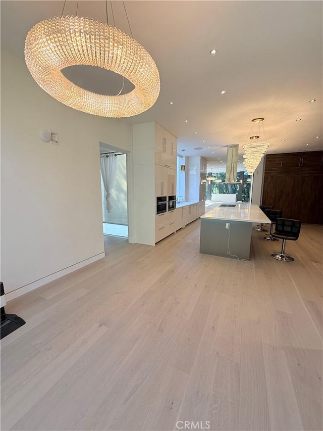 kitchen with a breakfast bar, white cabinetry, decorative light fixtures, a large island, and light hardwood / wood-style floors