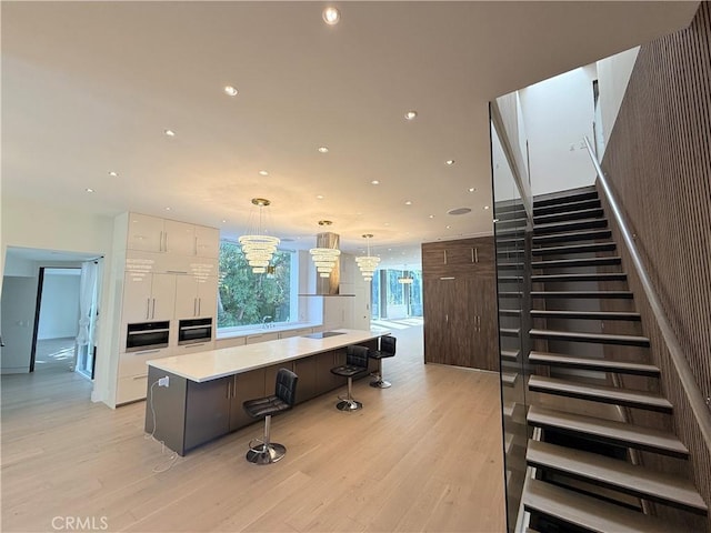 kitchen featuring white cabinetry, a spacious island, a notable chandelier, decorative light fixtures, and light wood-type flooring