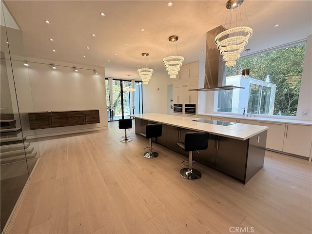 interior space featuring white cabinetry, island range hood, a chandelier, pendant lighting, and a large island