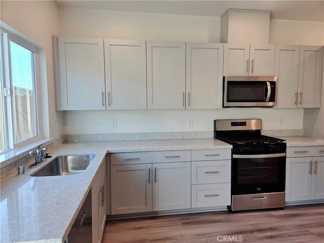 kitchen featuring sink, appliances with stainless steel finishes, white cabinetry, light stone counters, and light wood-type flooring