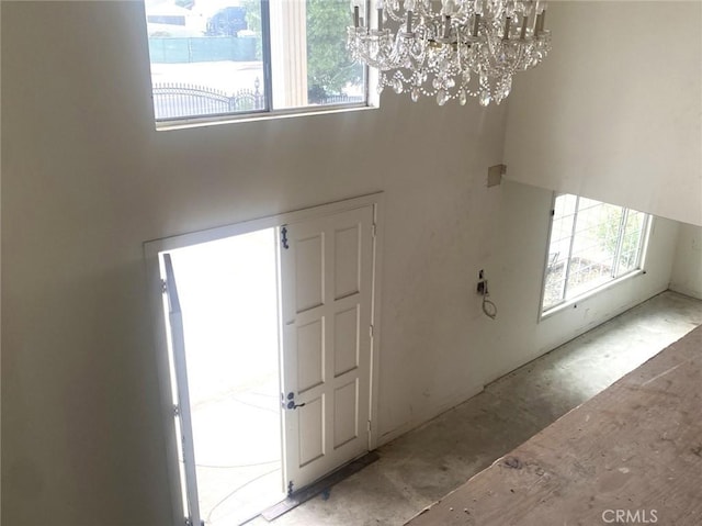 foyer with concrete flooring, a towering ceiling, and a notable chandelier