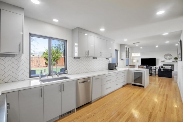 kitchen featuring sink, light wood-type flooring, dishwasher, kitchen peninsula, and backsplash