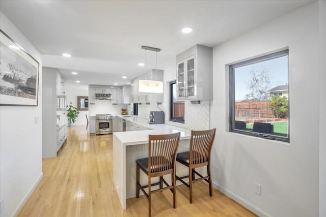 kitchen with white cabinets, a kitchen breakfast bar, hanging light fixtures, stainless steel range, and kitchen peninsula