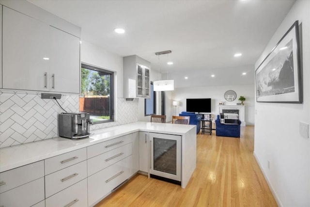 kitchen with hanging light fixtures, wine cooler, light hardwood / wood-style floors, white cabinets, and kitchen peninsula