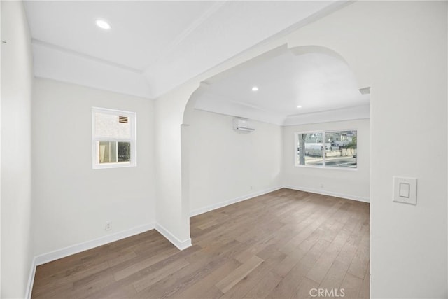 empty room with a wealth of natural light, a wall mounted air conditioner, and hardwood / wood-style floors