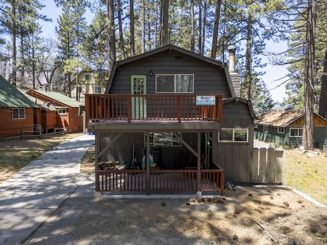 rear view of property with a gambrel roof, a wooden deck, and board and batten siding