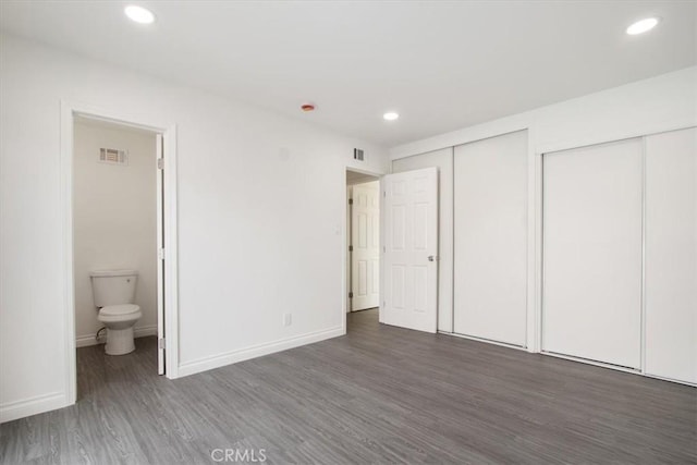 unfurnished bedroom with dark wood-type flooring, multiple closets, and ensuite bathroom