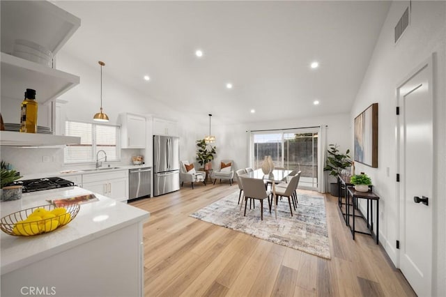 kitchen with lofted ceiling, sink, hanging light fixtures, stainless steel appliances, and white cabinets