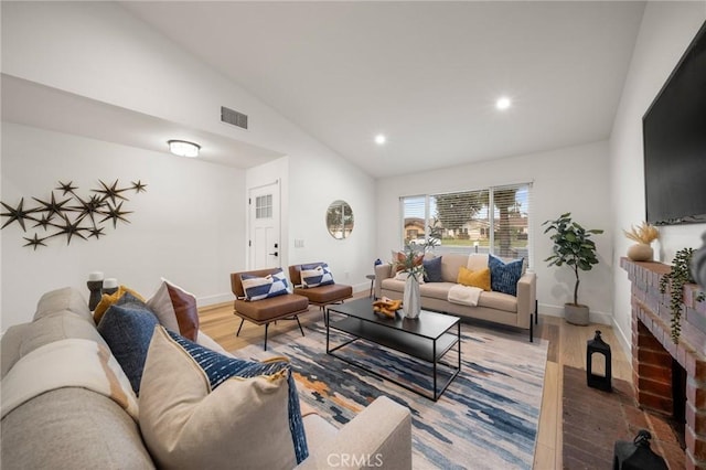 living room featuring high vaulted ceiling, hardwood / wood-style floors, and a brick fireplace