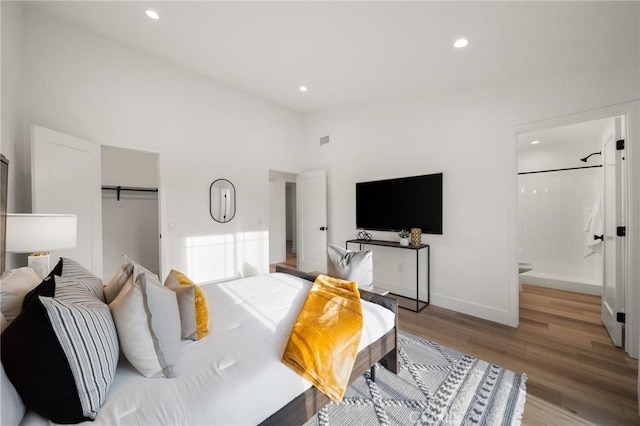 bedroom with a closet, connected bathroom, high vaulted ceiling, and light hardwood / wood-style flooring