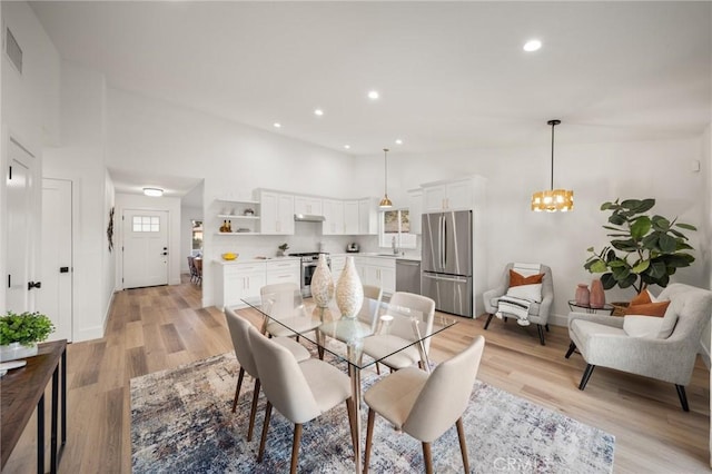 dining room with a notable chandelier, sink, a high ceiling, and light wood-type flooring