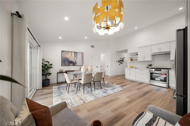 dining room with high vaulted ceiling, light wood-type flooring, and an inviting chandelier