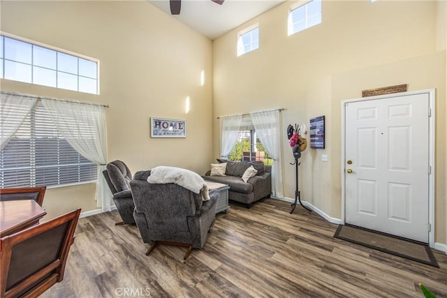 living room featuring hardwood / wood-style flooring, ceiling fan, and a towering ceiling