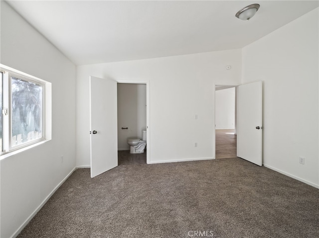 unfurnished bedroom featuring dark colored carpet, vaulted ceiling, and ensuite bath