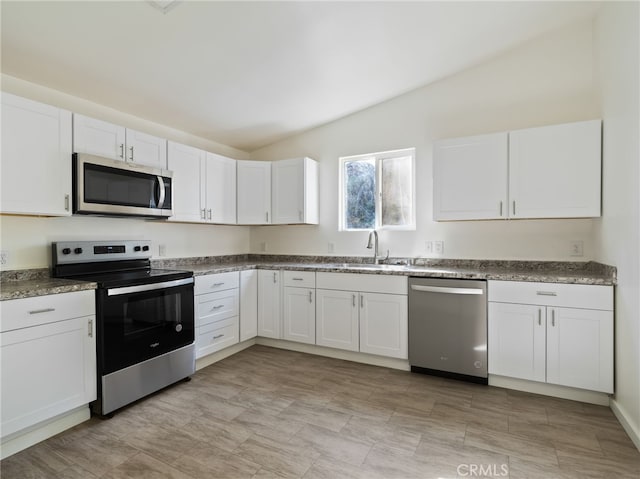 kitchen with sink, vaulted ceiling, stainless steel appliances, and white cabinets