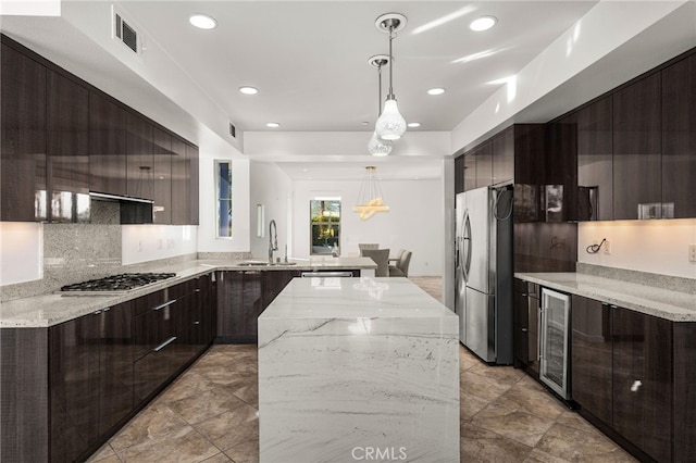 kitchen featuring sink, light stone counters, decorative light fixtures, stainless steel appliances, and beverage cooler