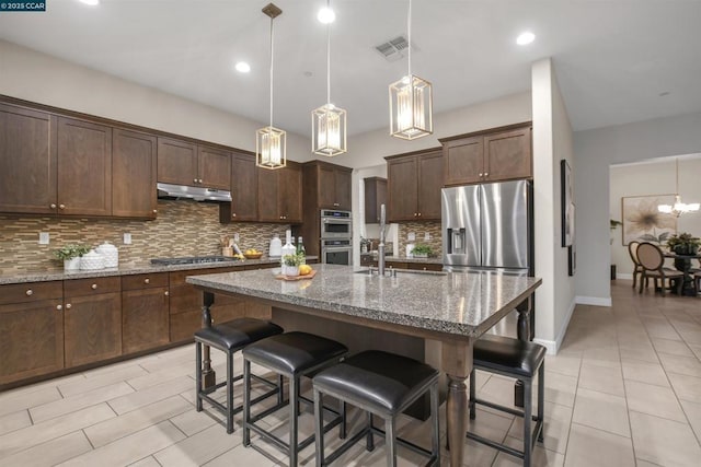 kitchen with stone countertops, a center island with sink, dark brown cabinetry, and appliances with stainless steel finishes