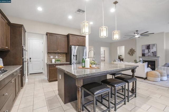 kitchen with appliances with stainless steel finishes, a kitchen island with sink, hanging light fixtures, light stone counters, and a kitchen bar