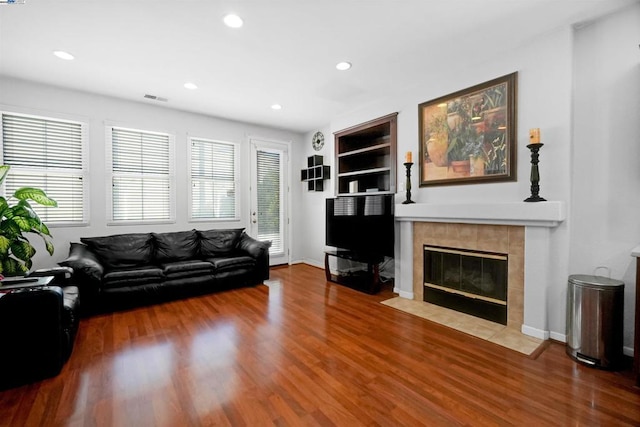 living room with built in shelves, a tiled fireplace, and hardwood / wood-style floors