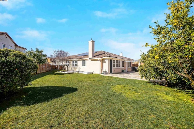 rear view of property with a lawn, a patio area, and solar panels